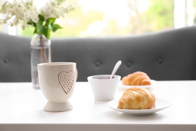 Photo of Cup and plate with tasty freshly baked croissant on table