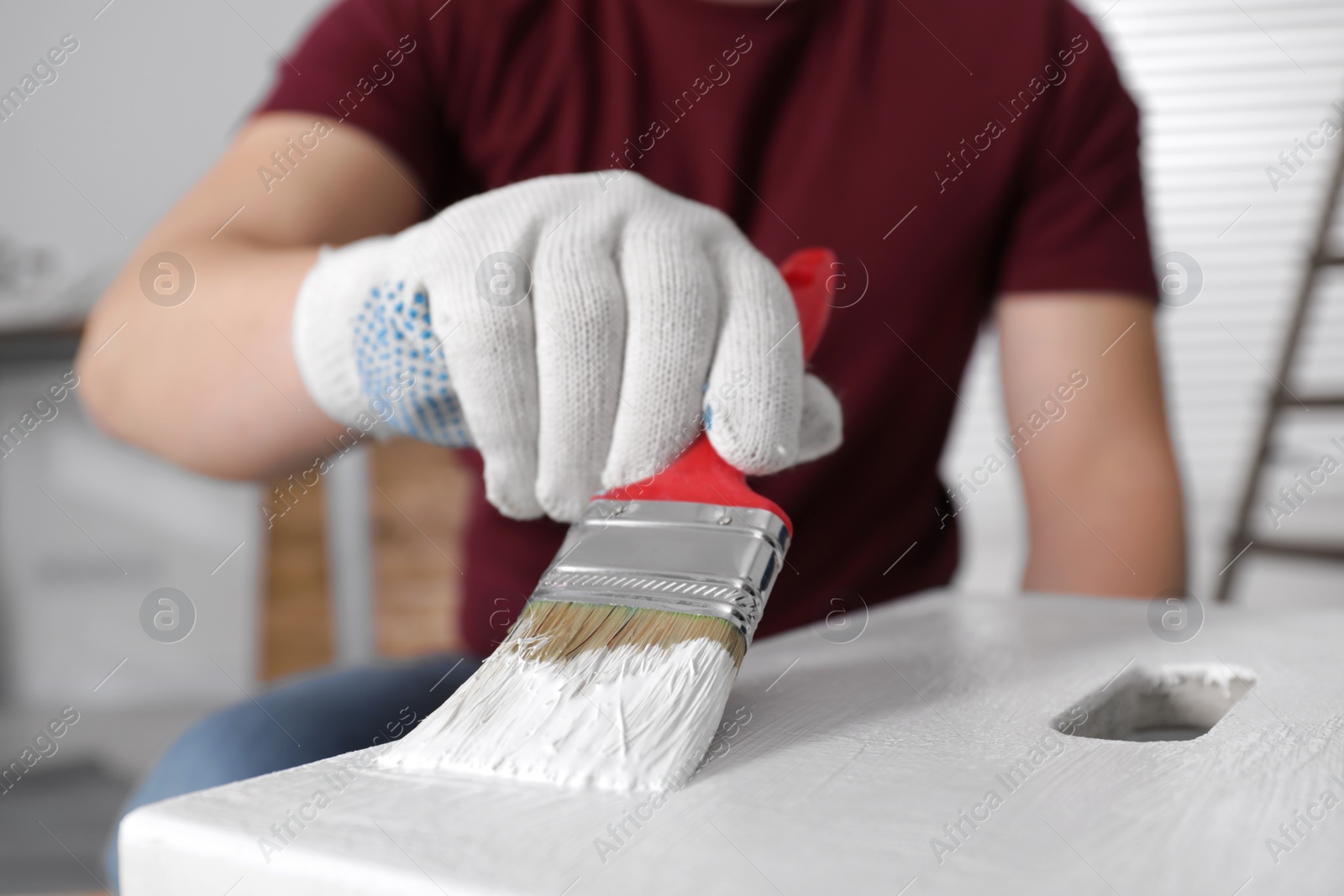 Photo of Man using brush to paint bekvam with white dye indoors, closeup