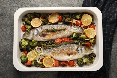 Photo of Delicious fish with vegetables and lemon in baking dish on grey textured table, top view