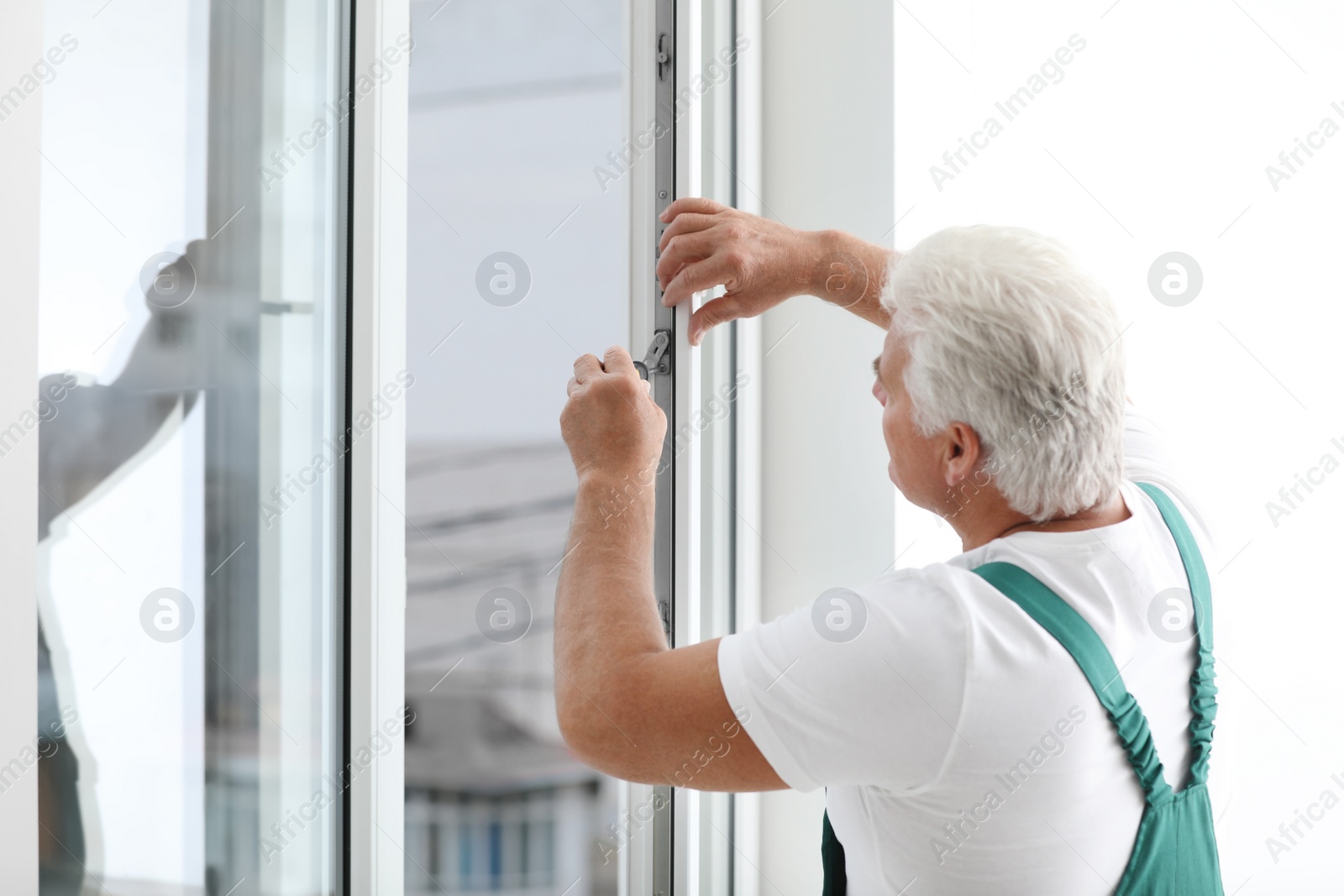 Photo of Mature construction worker repairing plastic window with screwdriver indoors