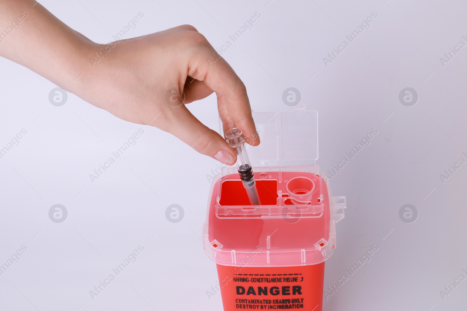 Photo of Woman throwing used syringe into sharps container on white background, closeup