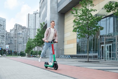 Happy man riding modern electric kick scooter on city street, space for text