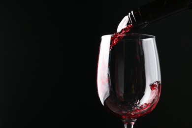 Photo of Pouring red wine into glass against black background, closeup. Space for text