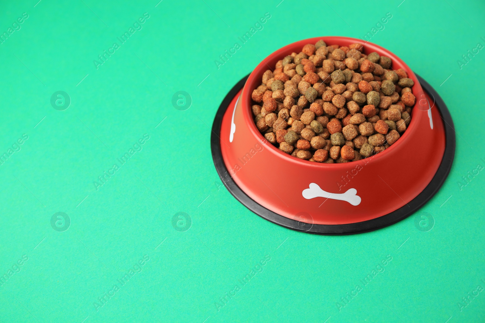 Photo of Dry dog food in feeding bowl on green background. Space for text