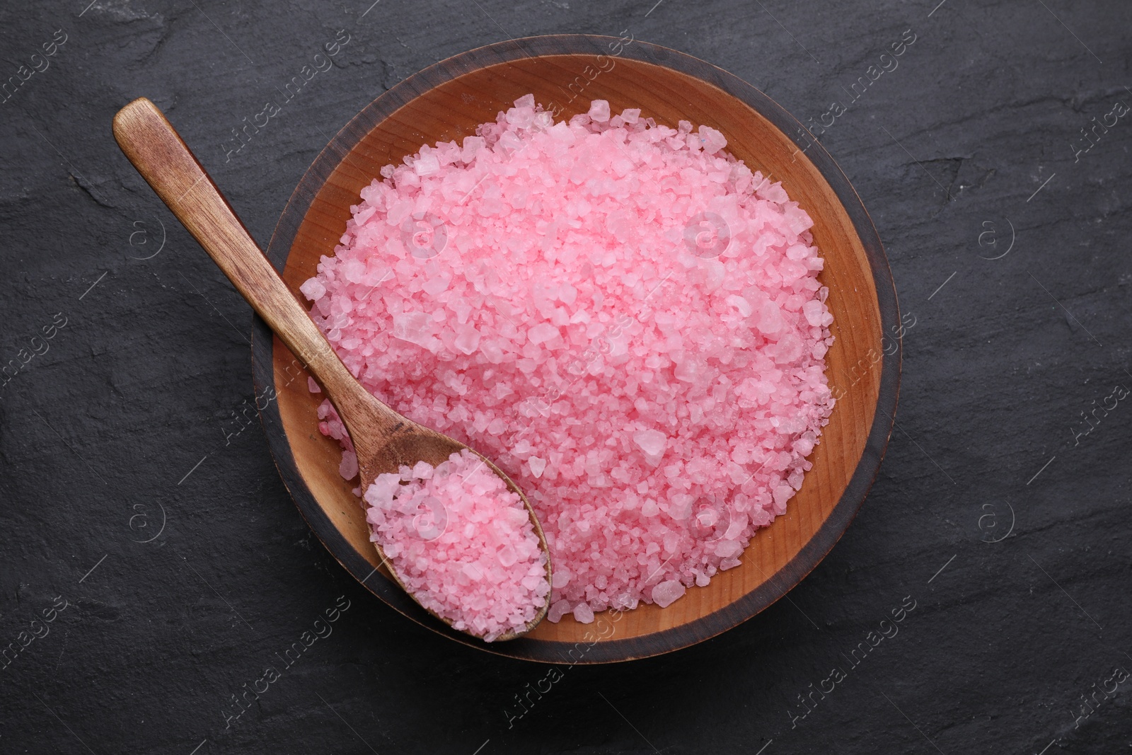 Photo of Bowl and spoon with pink sea salt on black table, top view