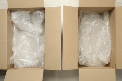 Photo of Open cardboard boxes with bubble wrap on white wooden floor, flat lay