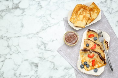 Photo of Tasty crepes with chocolate paste and berries served on white marble table, flat lay. Space for text