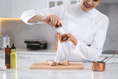 Photo of Professional chef adding pepper to delicious meat at white marble table, closeup