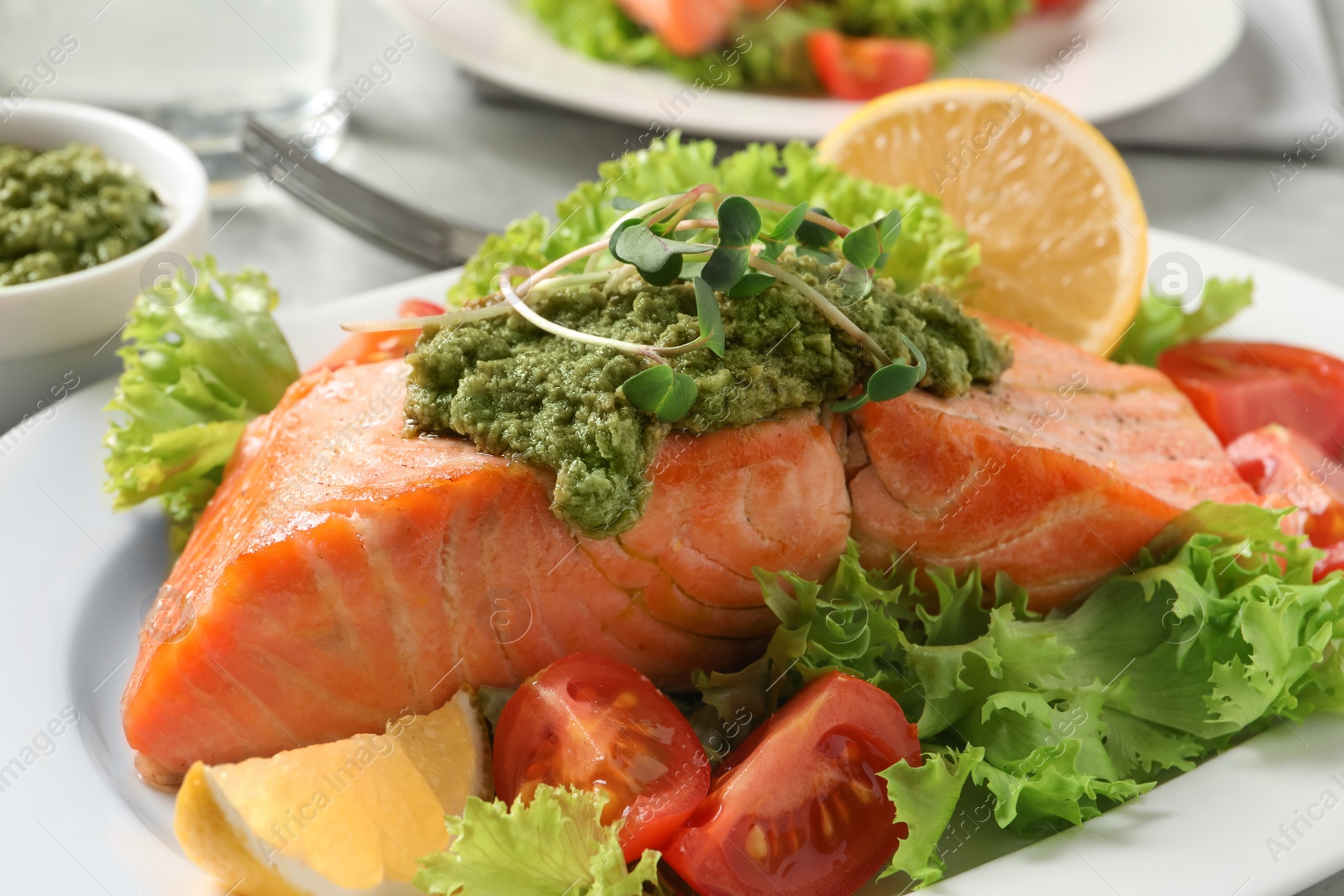 Photo of Tasty cooked salmon with pesto sauce and fresh salad on plate, closeup