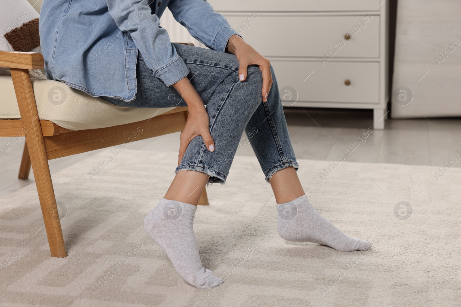 Photo of Woman suffering from leg pain on armchair at home, closeup