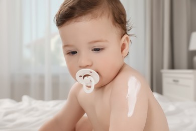 Cute little baby with cream on arm indoors