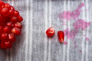 Photo of Striped shirt with fruit juicy stains and pomegranate seeds as background, top view