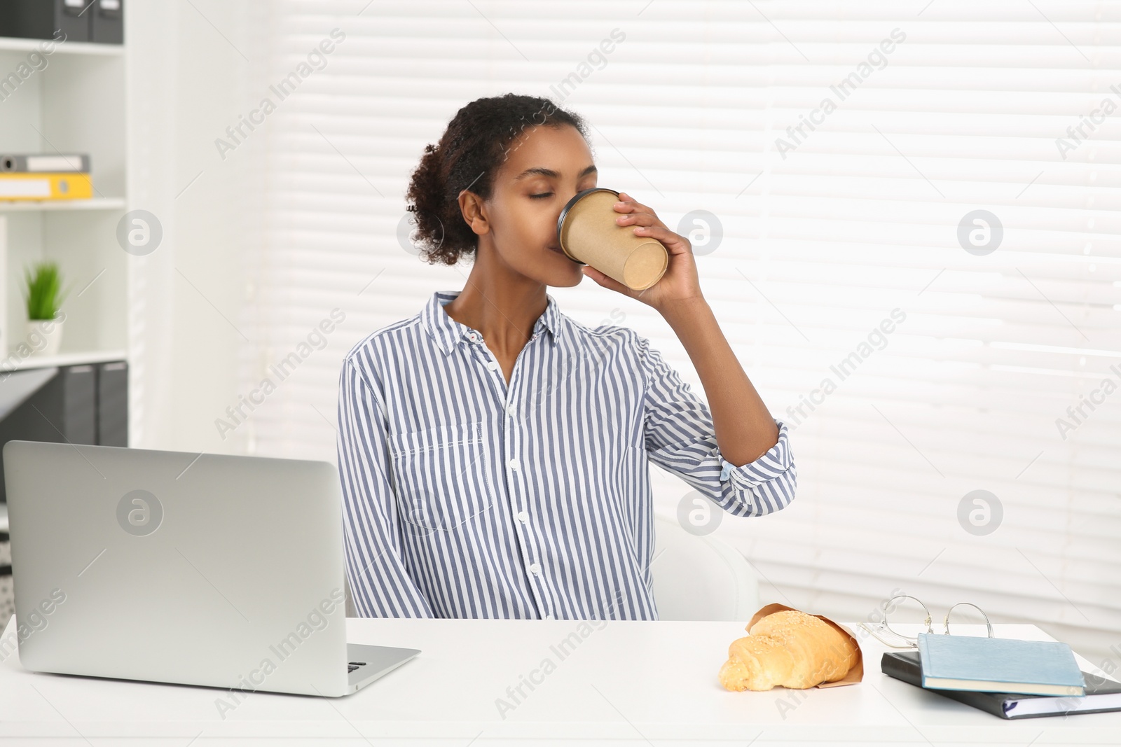 Photo of African American intern drinking coffee at white table in office