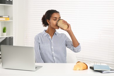 African American intern drinking coffee at white table in office