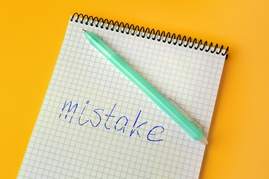 Photo of Word Mistake written with erasable pen in notepad on yellow background, above view