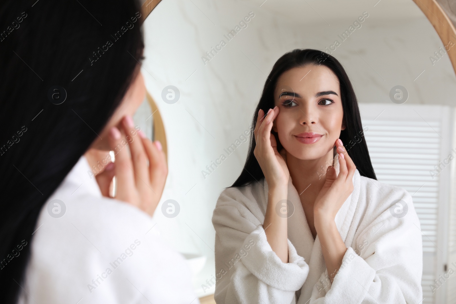 Photo of Beautiful young woman looking at herself in bathroom mirror