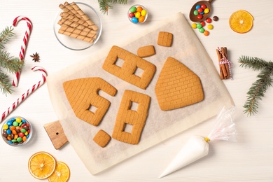 Photo of Parts of gingerbread house and ingredients for decoration on white wooden table, flat lay