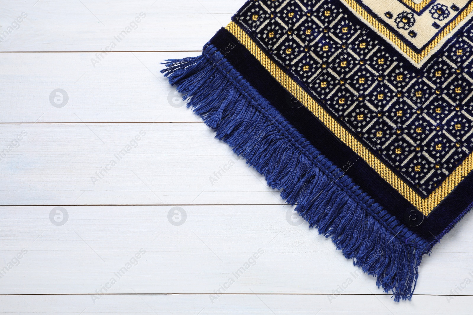 Photo of Muslim prayer rug on white wooden table, top view. Space for text