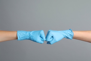 Doctors in medical gloves making fist bump on grey background, closeup