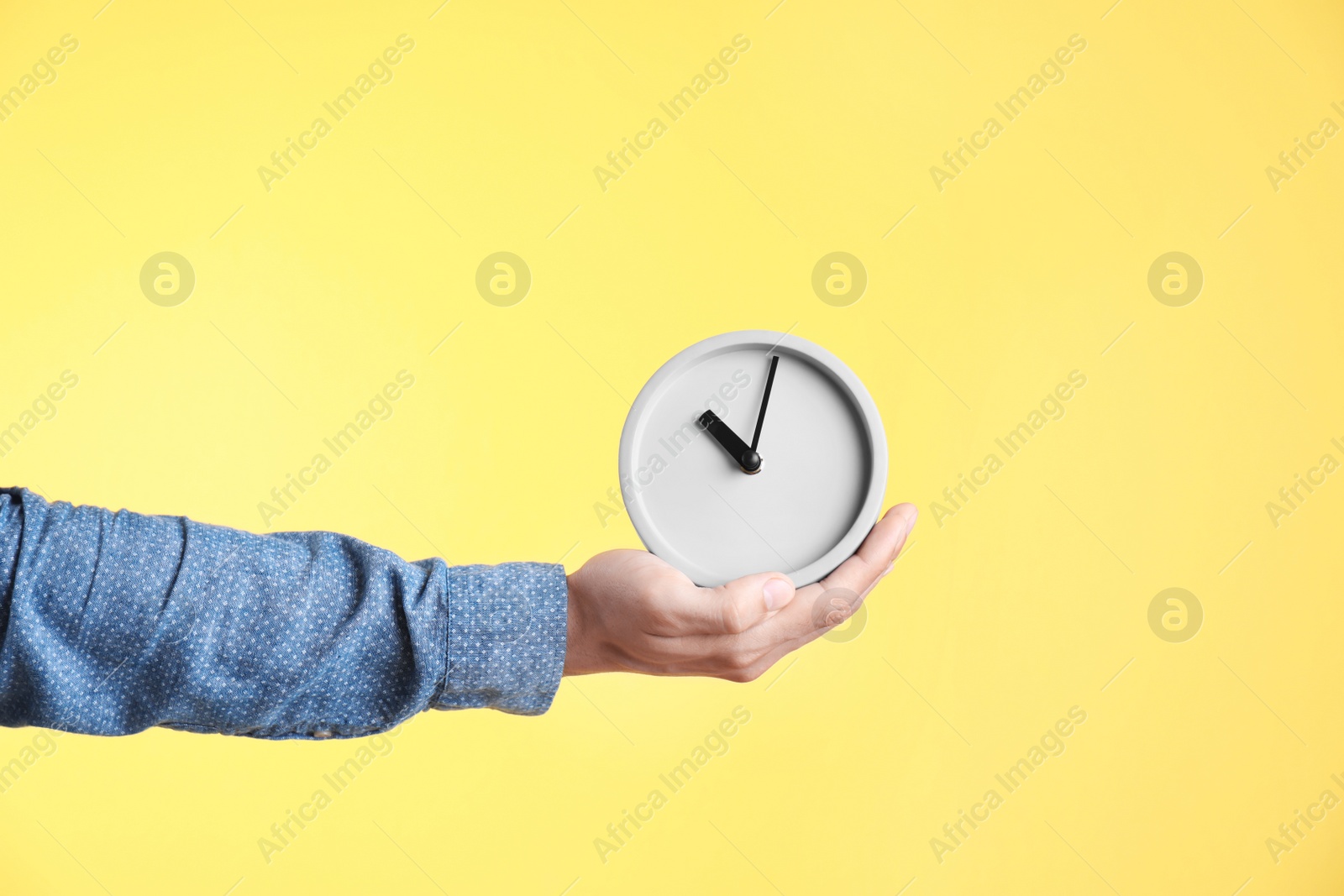 Photo of Young man holding clock on color background. Time management