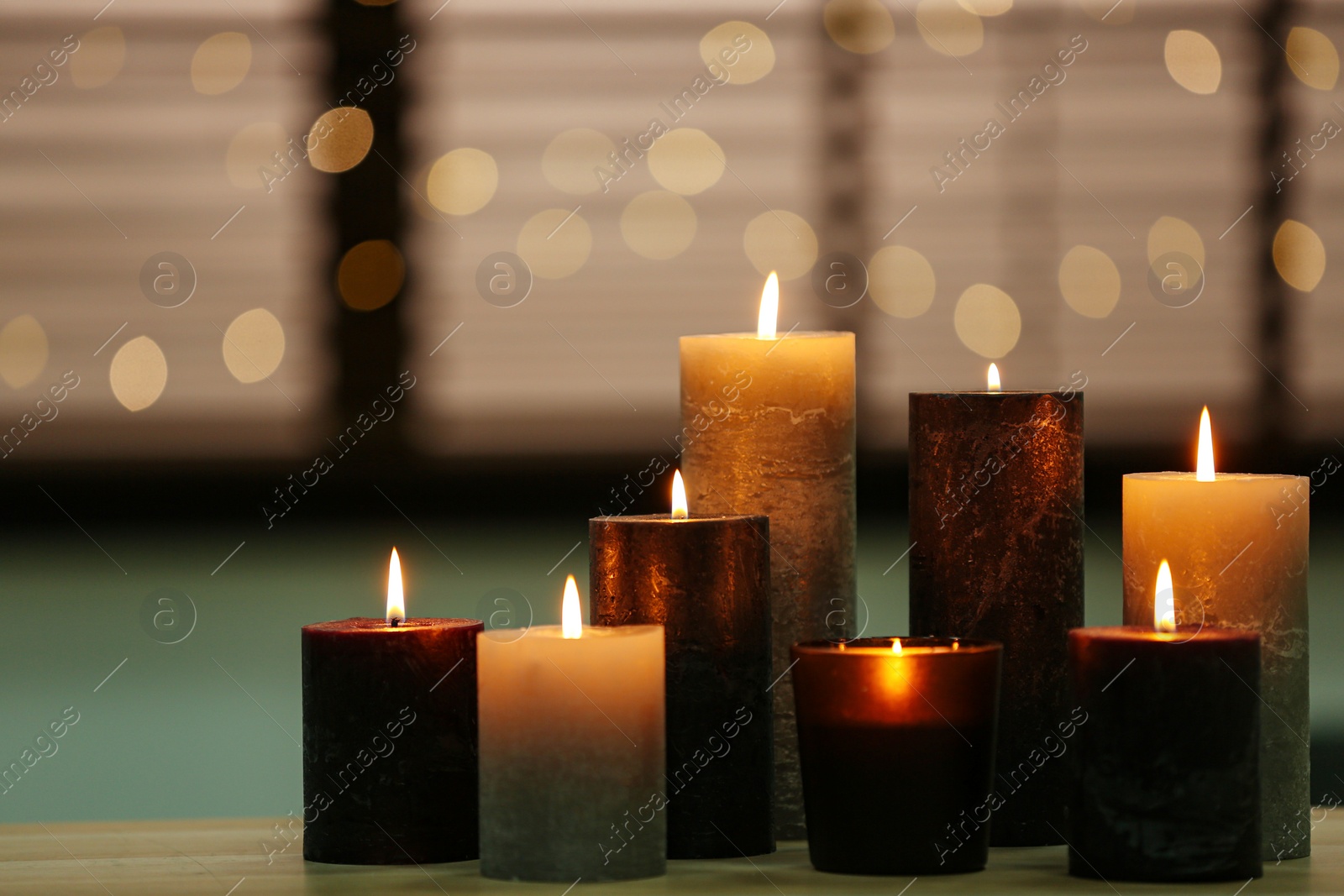 Photo of Beautiful burning candles on wooden table against festive lights. Space for text