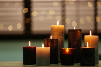 Photo of Beautiful burning candles on wooden table against festive lights. Space for text