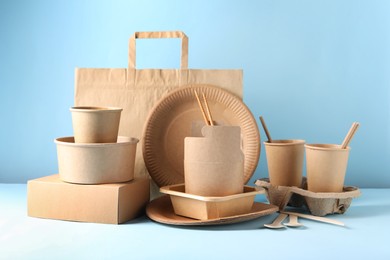 Photo of Eco friendly food packaging. Paper containers, tableware and bag on white table against light blue background