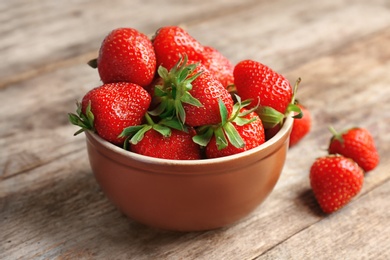 Photo of Bowl with ripe red strawberries on wooden table