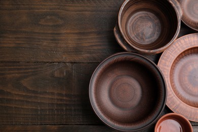 Set of clay dishes on wooden table, flat lay with space for text. Cooking utensils