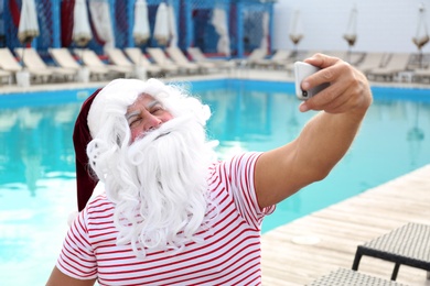 Photo of Authentic Santa Claus taking selfie near swimming pool outdoors