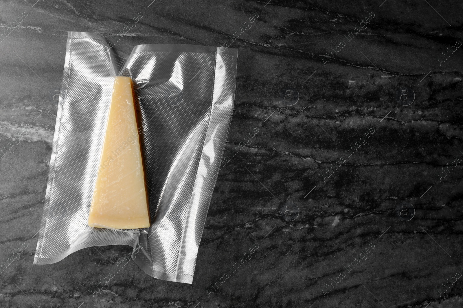 Photo of Cheese in vacuum pack on black marble table, top view. Space for text