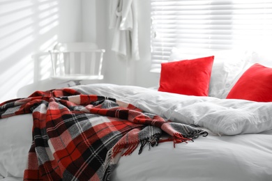 Photo of Comfortable bed with warm checkered plaid in stylish room interior