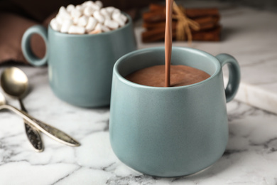 Pouring hot cocoa drink into cup on white marble table