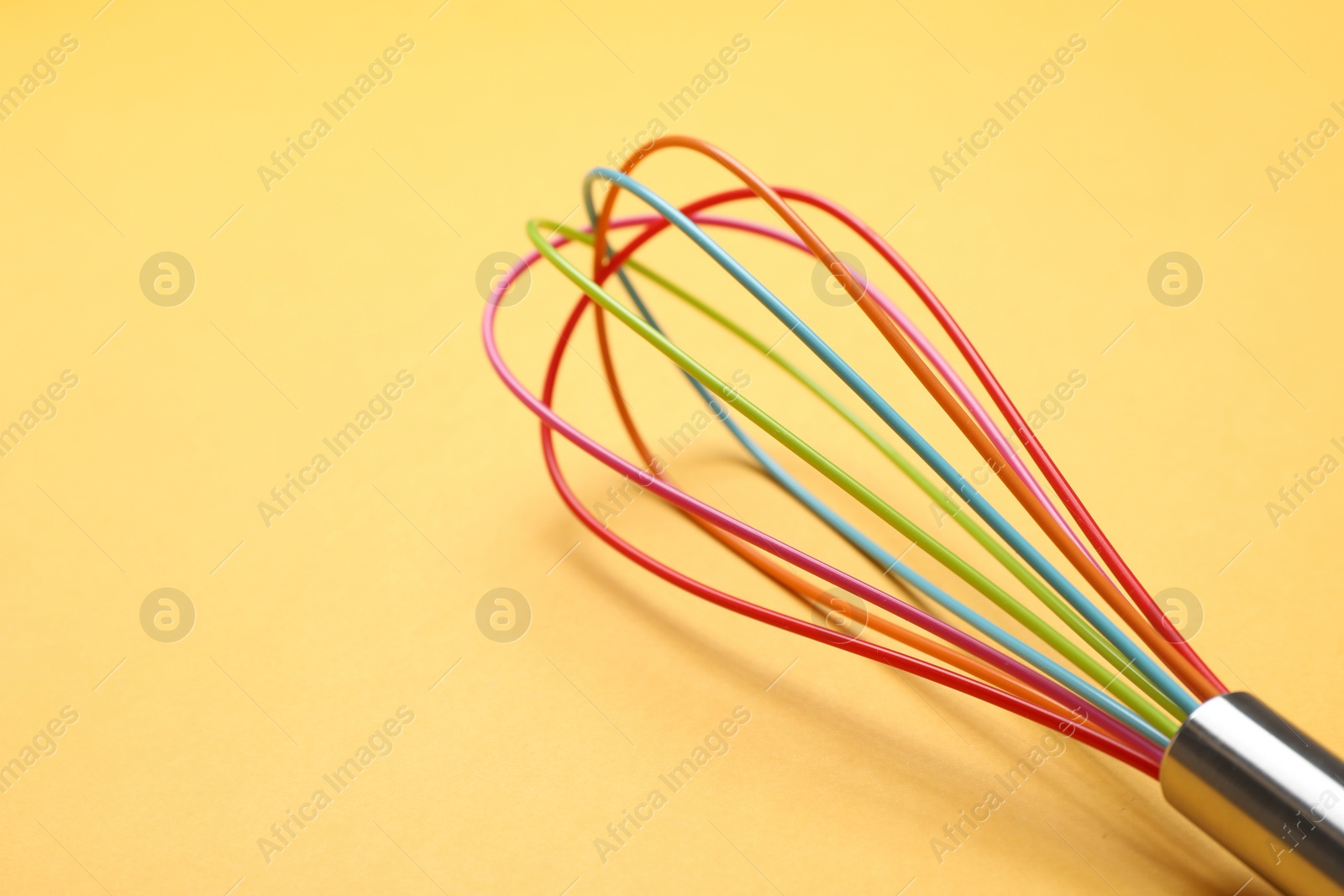 Photo of Bright whisk on yellow background, closeup. Space for text