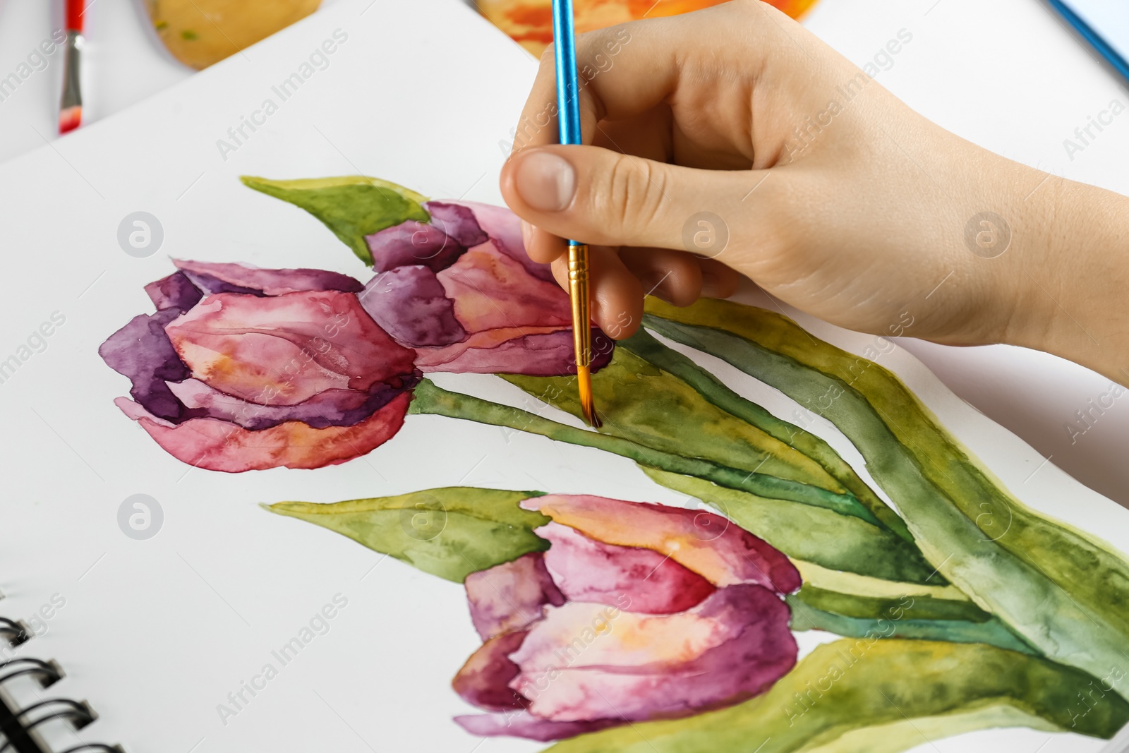 Photo of Woman painting tulips in sketchbook, closeup view