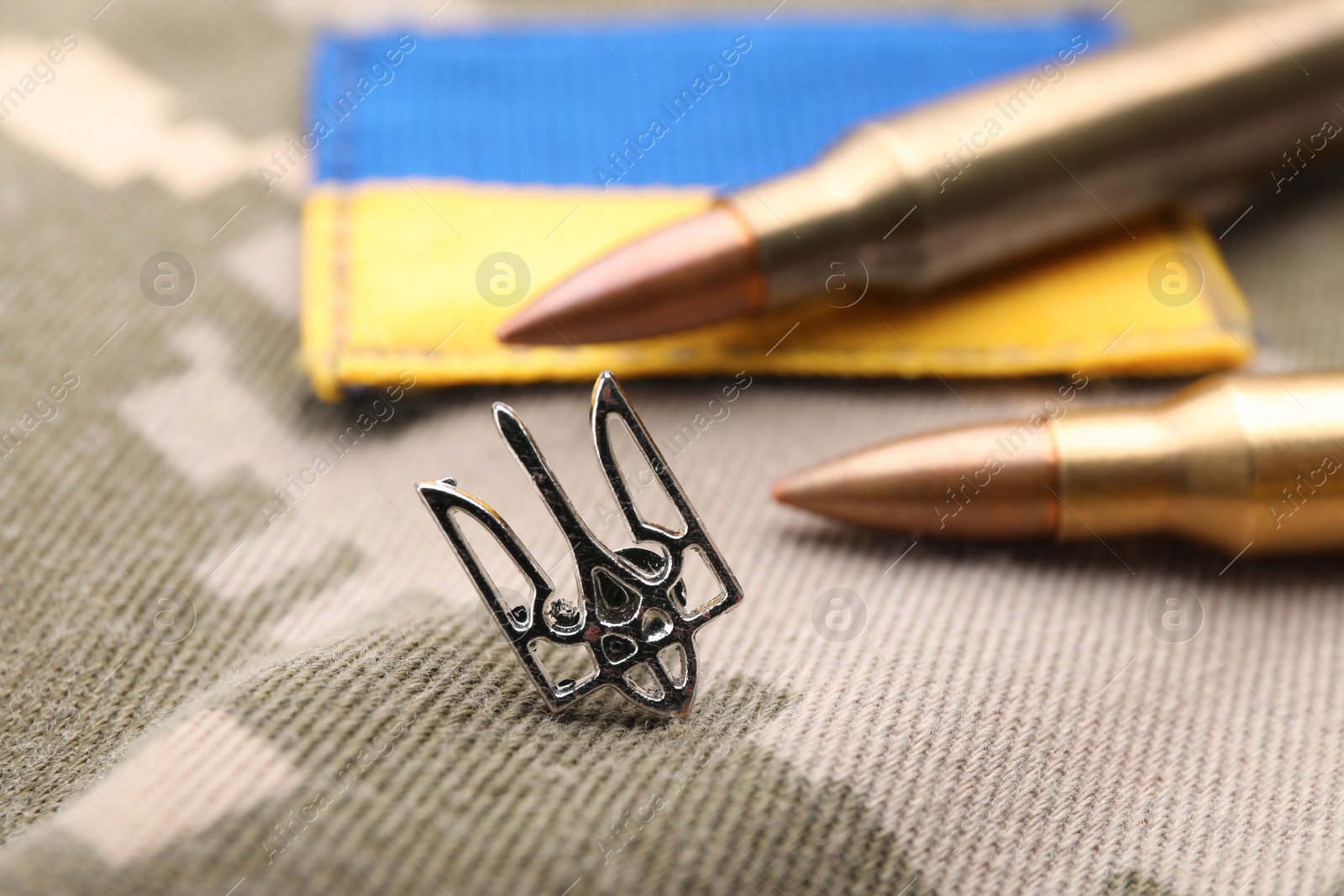 Photo of Ukrainian trident near army patch and bullets on camouflage background, closeup