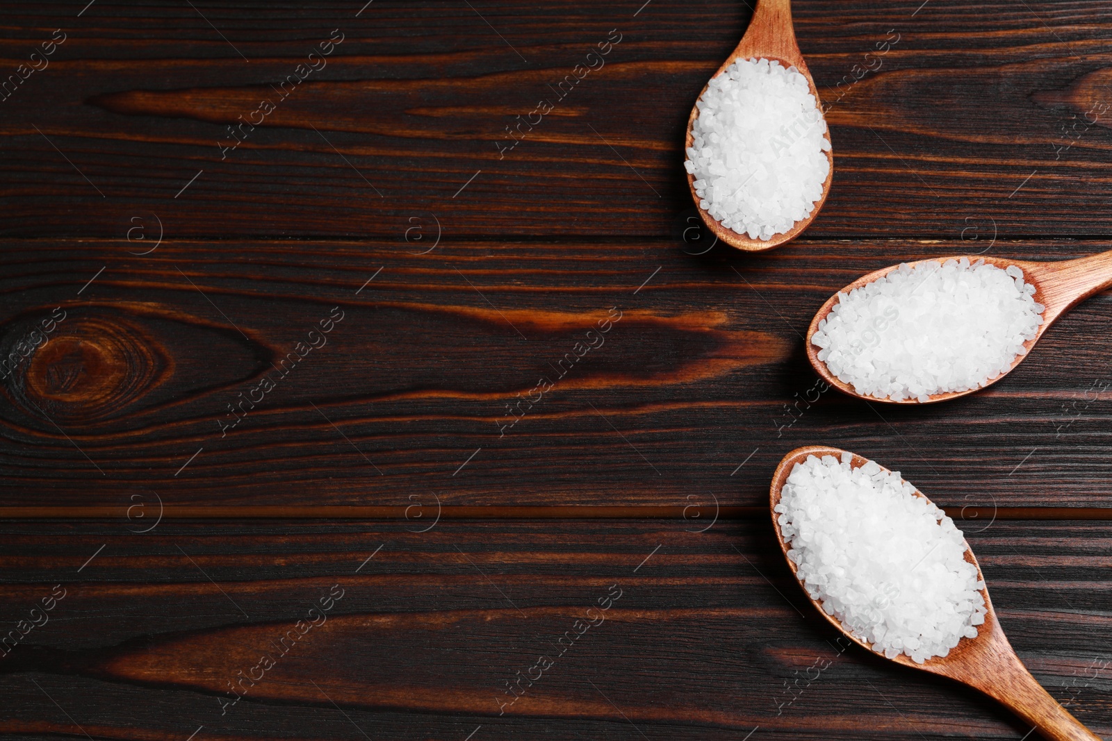 Photo of Spoons with natural sea salt on wooden table, flat lay. Space for text