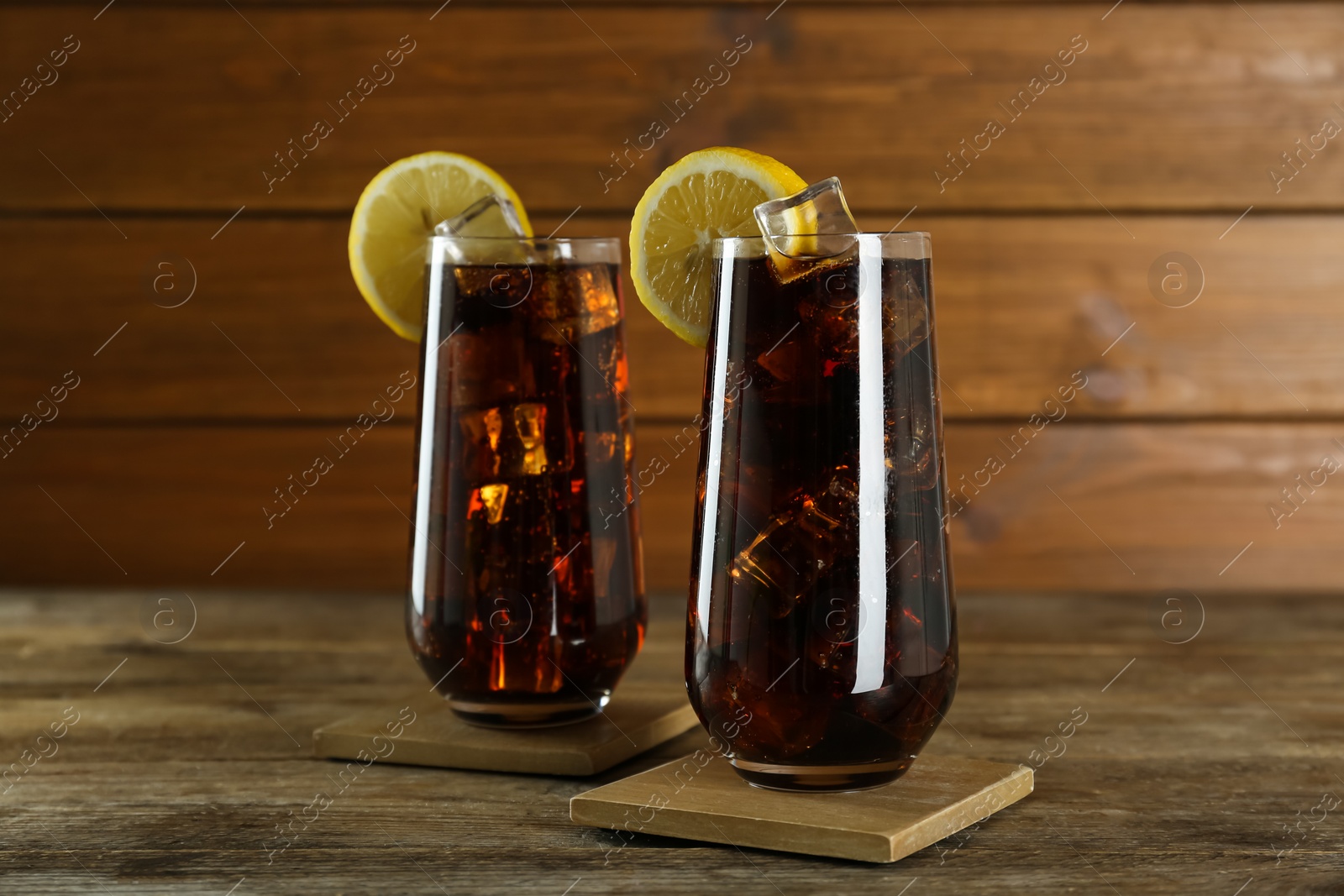Photo of Glasses of refreshing soda water with ice cubes and lemon slices on wooden table