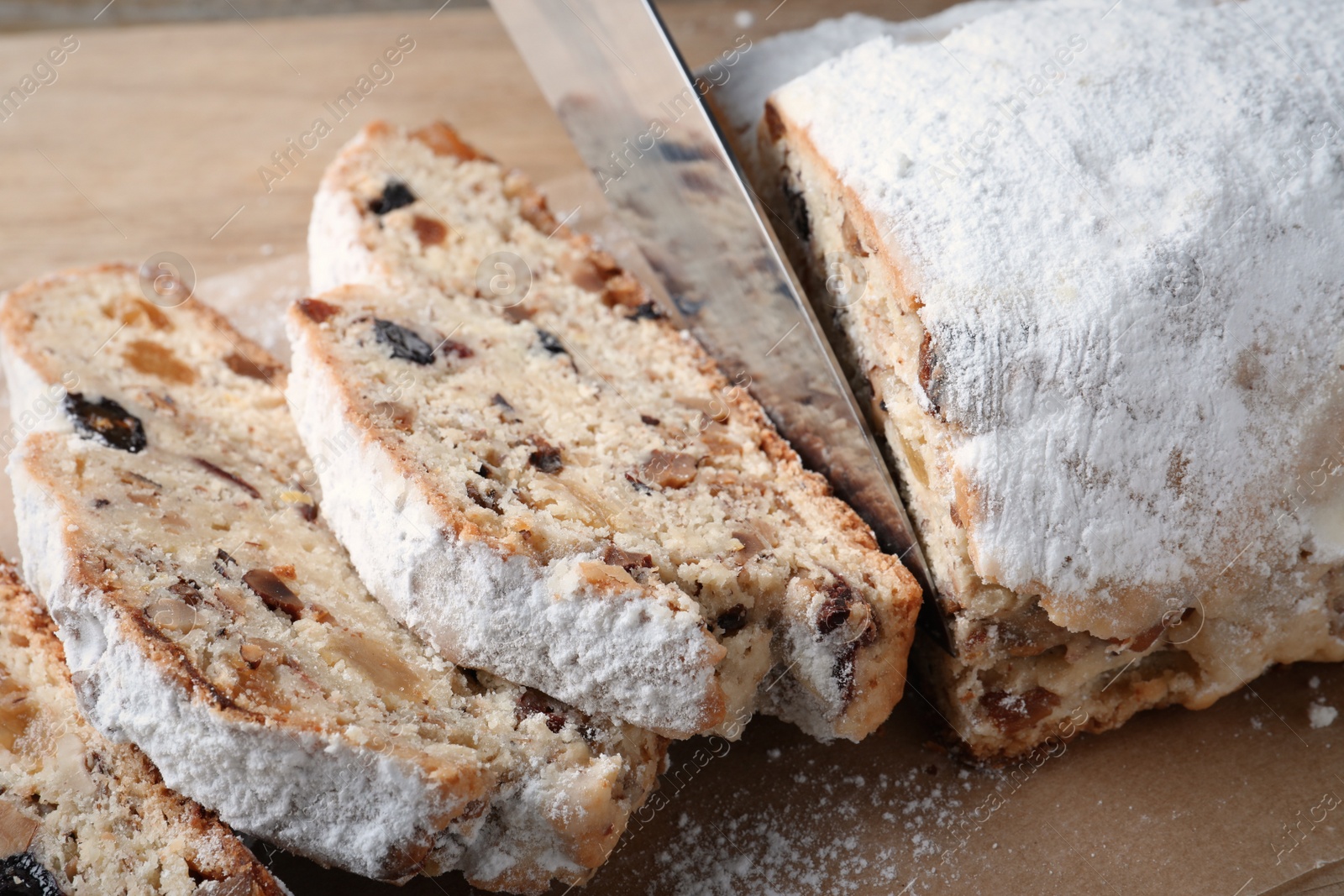 Photo of Cutting traditional Christmas Stollen with knife on parchment paper, closeup