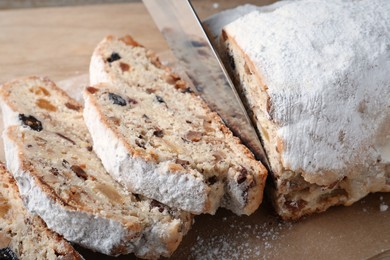 Photo of Cutting traditional Christmas Stollen with knife on parchment paper, closeup