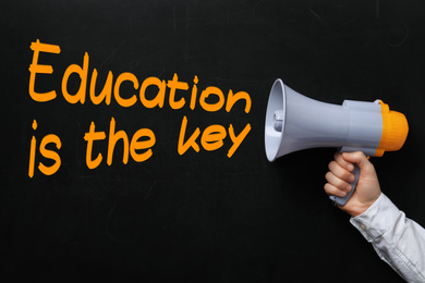 Man holding megaphone near chalkboard with phrase Education is the key, closeup. Adult learning