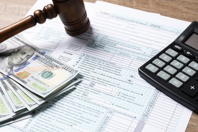 Photo of Tax return forms, dollar banknotes, calculator and gavel on wooden table, closeup