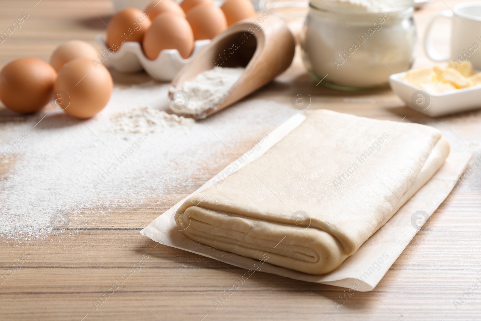 Photo of Parchment with puff pastry dough on wooden table, space for text