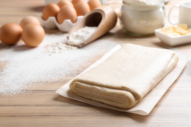 Photo of Parchment with puff pastry dough on wooden table, space for text