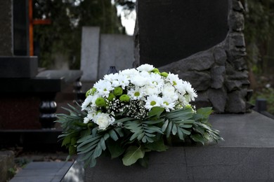 Photo of Funeral wreath of flowers on granite tombstone in cemetery