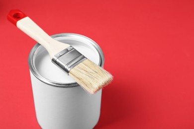 Photo of Can of white paint with brush on red background. Space for text