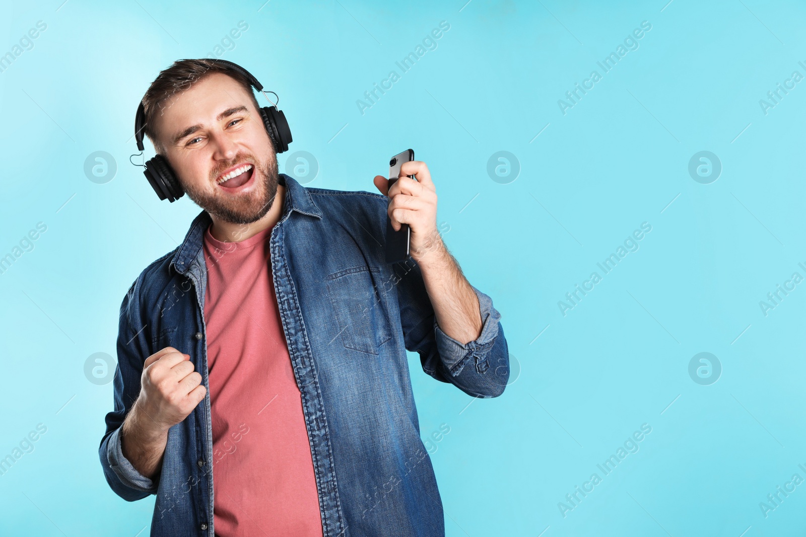 Photo of Handsome man with mobile phone enjoying music in headphones on color background. Space for text