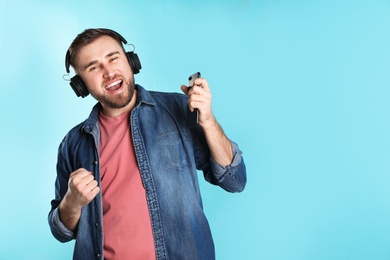 Handsome man with mobile phone enjoying music in headphones on color background. Space for text