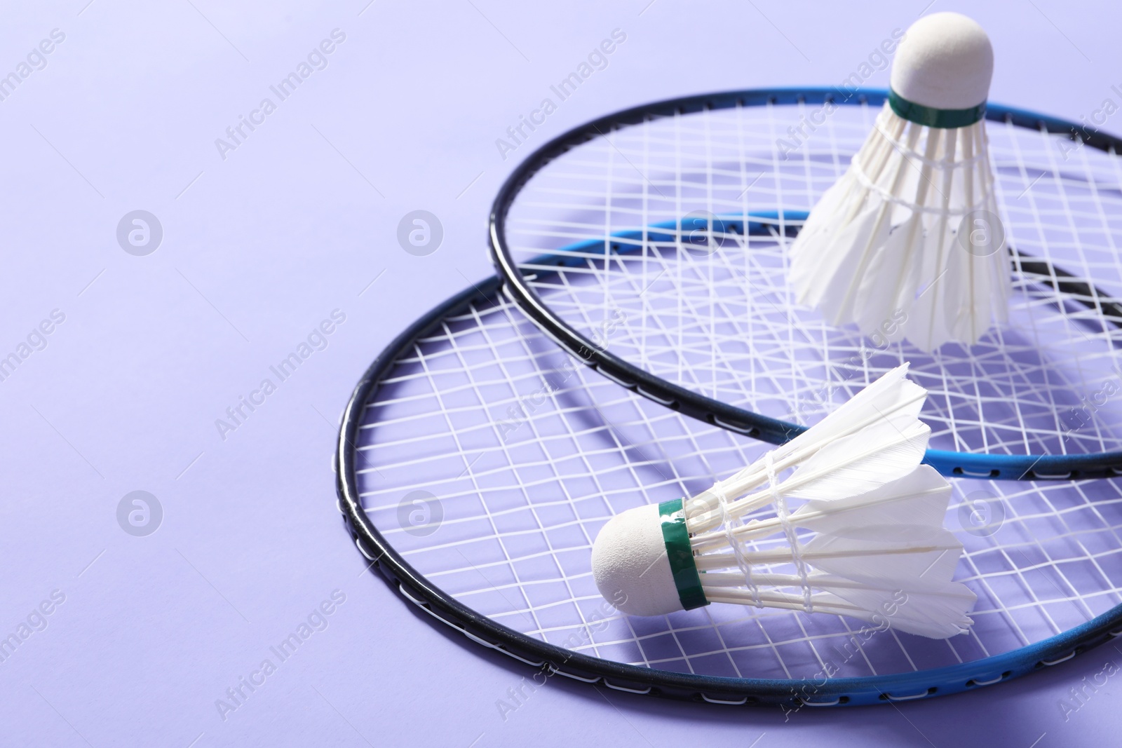 Photo of Feather badminton shuttlecocks and rackets on violet background, closeup. Space for text