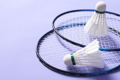 Feather badminton shuttlecocks and rackets on violet background, closeup. Space for text